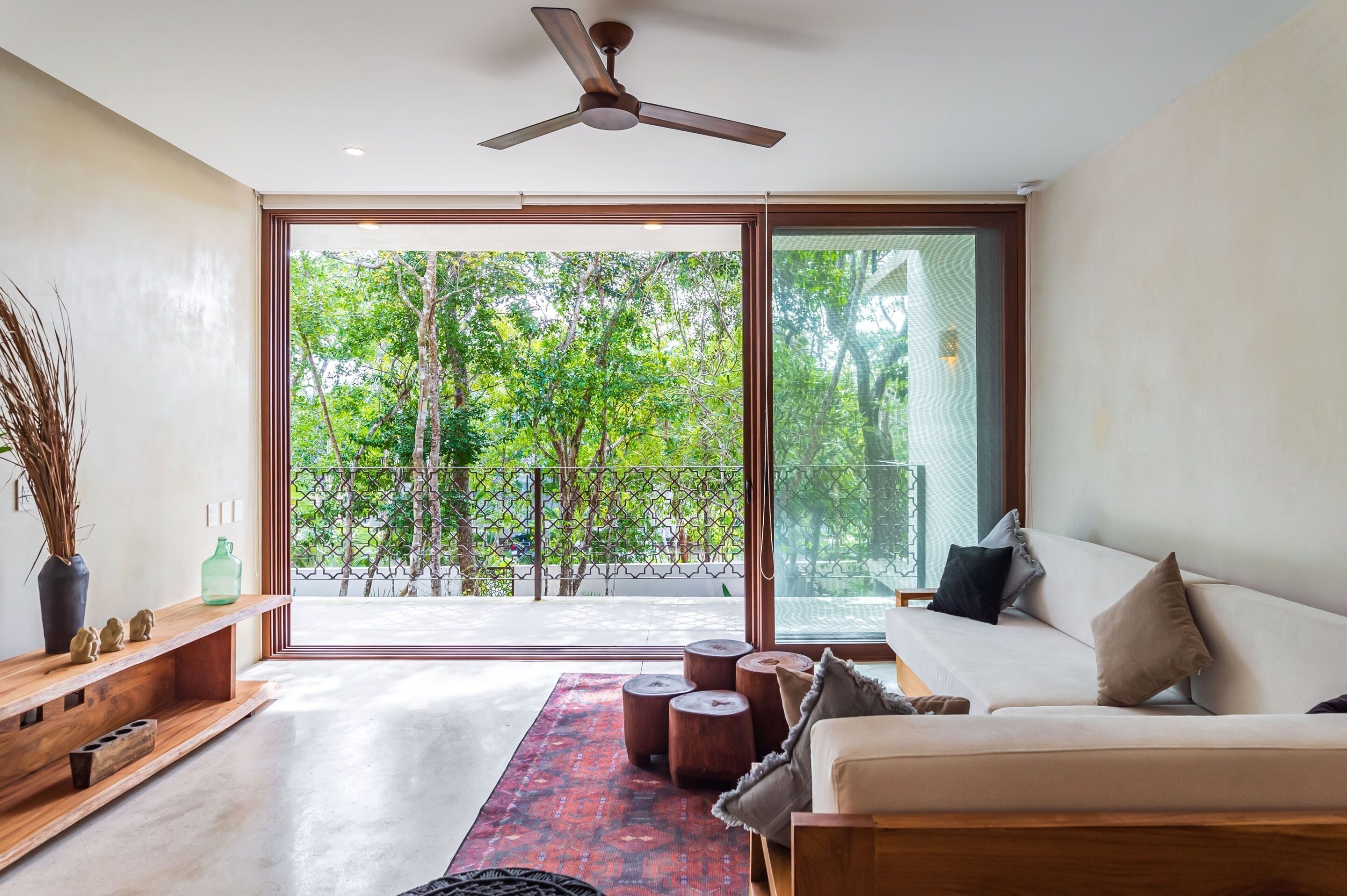 A modern living room with a sofa, wooden coffee table, and a large sliding glass door leading to a balcony with trees.