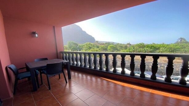 A balcony with a table and chairs, a stone balustrade, and a view of a mountain and greenery. - Yuremar La Puntilla Apt  3 (Valle Gran Rey)