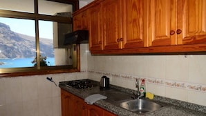 Eine Küche mit Holzschränken, einer Granit-Arbeitsplatte, einem Edelstahl-Spülbecken und einem Fenster mit Blick auf eine gebirgige Landschaft.
