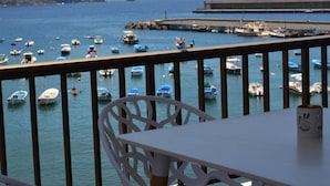 Ein Balkon mit Blick auf einen Hafen voller Boote, eine felsige Küste und einen Steg.