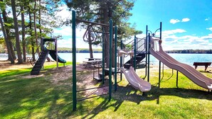 Ein Spielplatz mit Rutschen und Klettergerüsten in der Nähe eines Sees.