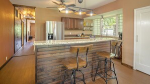 A kitchen with a central island, bar stools, a ceiling fan, and a window with a view. - Whippoorwill Hill: Easy Access Guadalupe Riverfront, Great Patios, Mins to Whitewater Amphitheater (Canyon Lake)