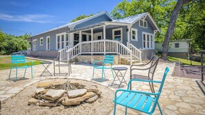 A house with a covered porch, stone patio, and outdoor seating area with chairs and a fire pit. - Whippoorwill Hill: Easy Access Guadalupe Riverfront, Great Patios, Mins to Whitewater Amphitheater (Canyon Lake)