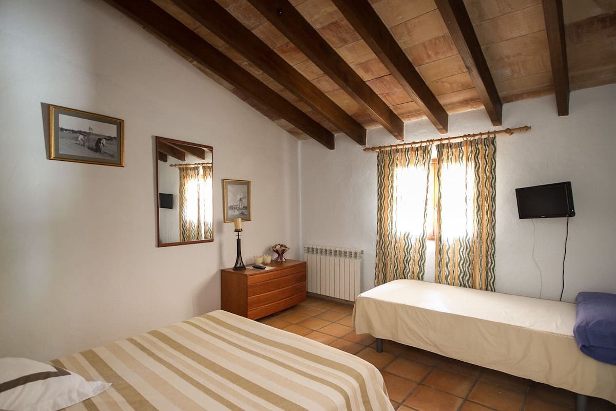 A bedroom with a bed, a dresser, a mirror, a television, and a window with curtains.