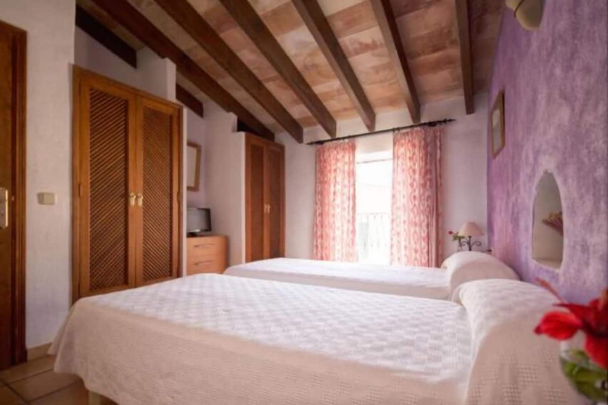 A bedroom with two beds, wooden beams on the ceiling, a wardrobe, and a window with curtains.