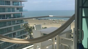 Ein Balkon mit Blick auf Strand und Meer, ein weißer Tisch mit Stühlen und eine Hängematte.