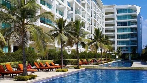 Ein modernes Hotel mit einem großen Schwimmbad, umgeben von Palmen und Liegestühlen.