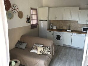 A compact living space with a sofa, a washing machine, a microwave, and a small kitchen area. - Cassiopeia quiet area  (Agde)