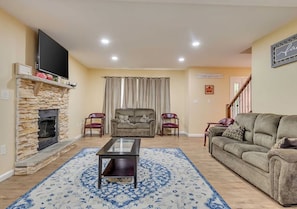 A living room with a stone fireplace, a flat-screen TV mounted above it, a patterned rug, two sofas, and a staircase in the background. - Vacation home near Kalahari Resort and Tobyhanna Lake (Tobyhanna)