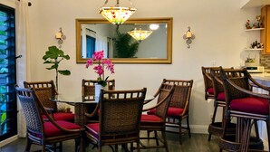 A dining area with wicker chairs and red cushions, a glass table, and a hanging light fixture. - Beautiful condo,air conditioning in bedrooms,ocean 100 yards from unit,sleeps 4 (Kapaa)
