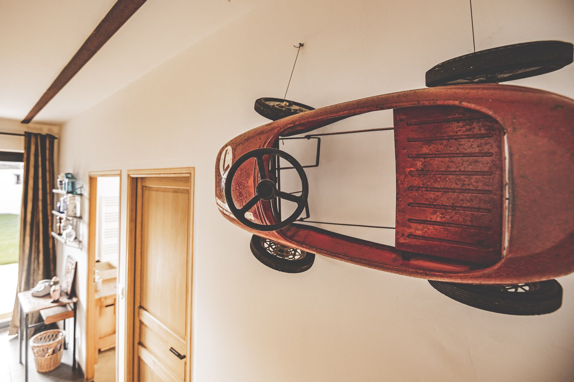 Ein altes Automodell an der Wand, eine Holztür und ein Korb auf dem Boden.