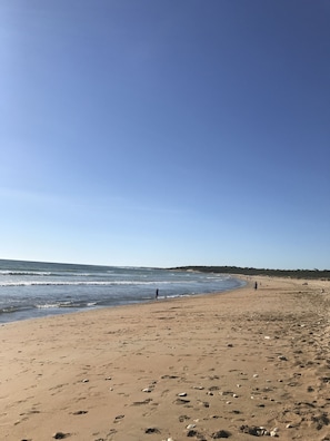 Ein Sandstrand mit Fußabdrücken und einigen Spaziergängern.