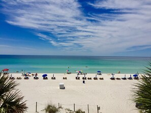 A beach with rows of sun loungers and umbrellas, a sandy shore, and a clear blue sky.