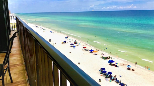 A balcony with a view of a beach, wooden floor, and a railing.
