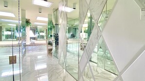 A modern lobby with reflective marble floors, glass partitions, and a central staircase.