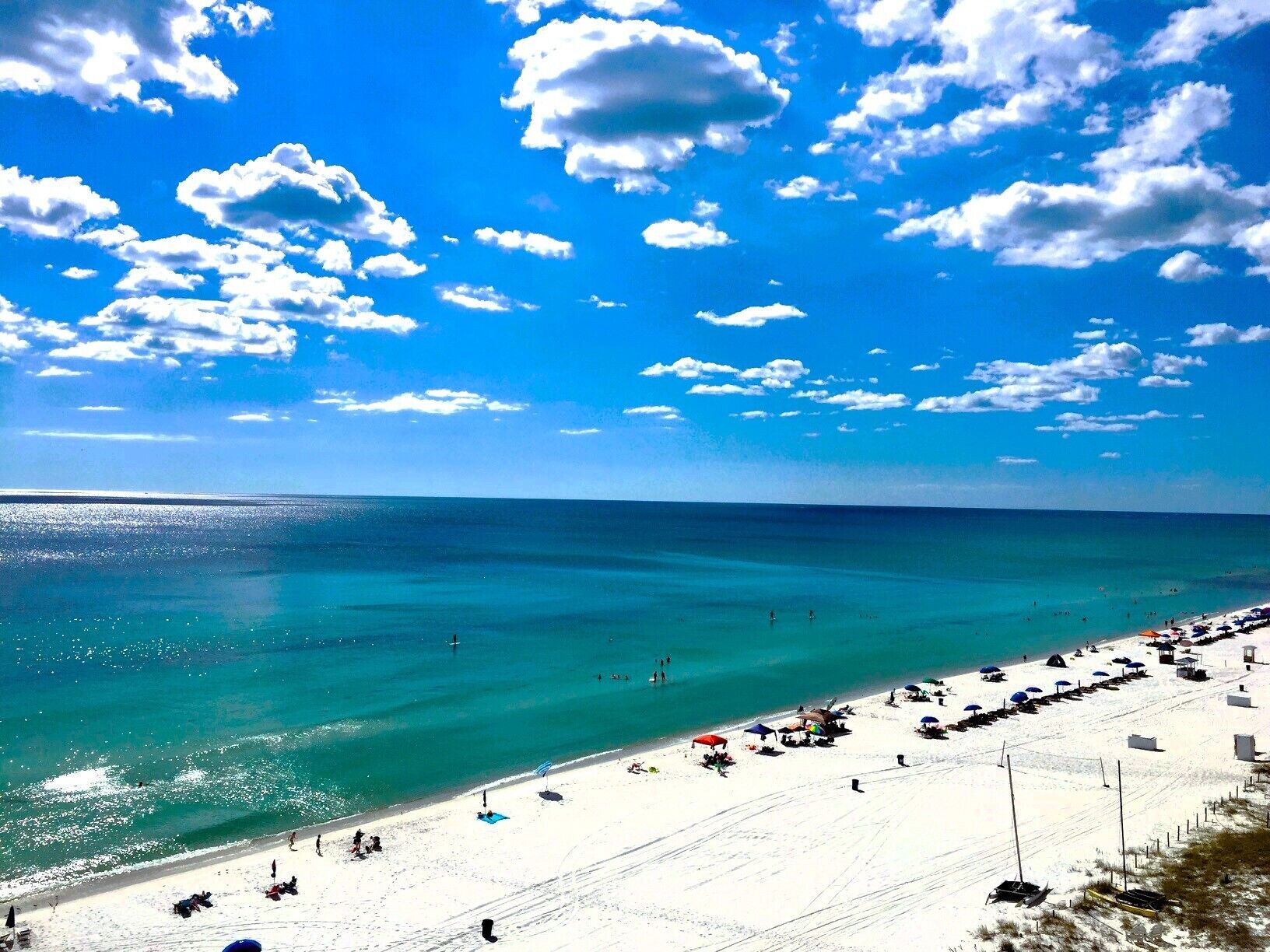 Une plage avec une eau turquoise et limpide, du sable blanc et quelques personnes.