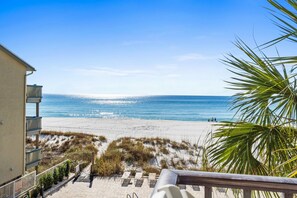 Strandudsigt fra en balkon med klart himmel, sandstrand og vegetation.