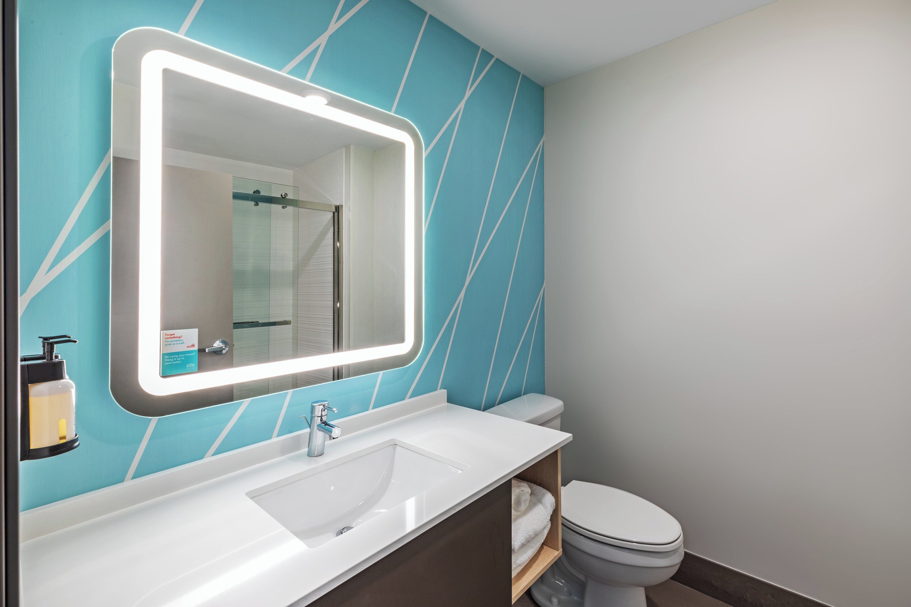 A bathroom with a white sink, a mirror with a light, and a toilet.