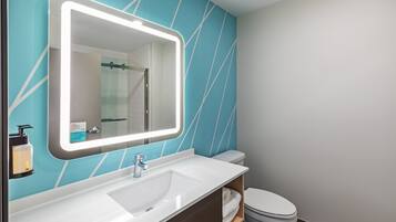 Une salle de bain avec un lavabo blanc, un miroir avec un éclairage intégré, des toilettes et un mur bleu orné de lignes blanches.