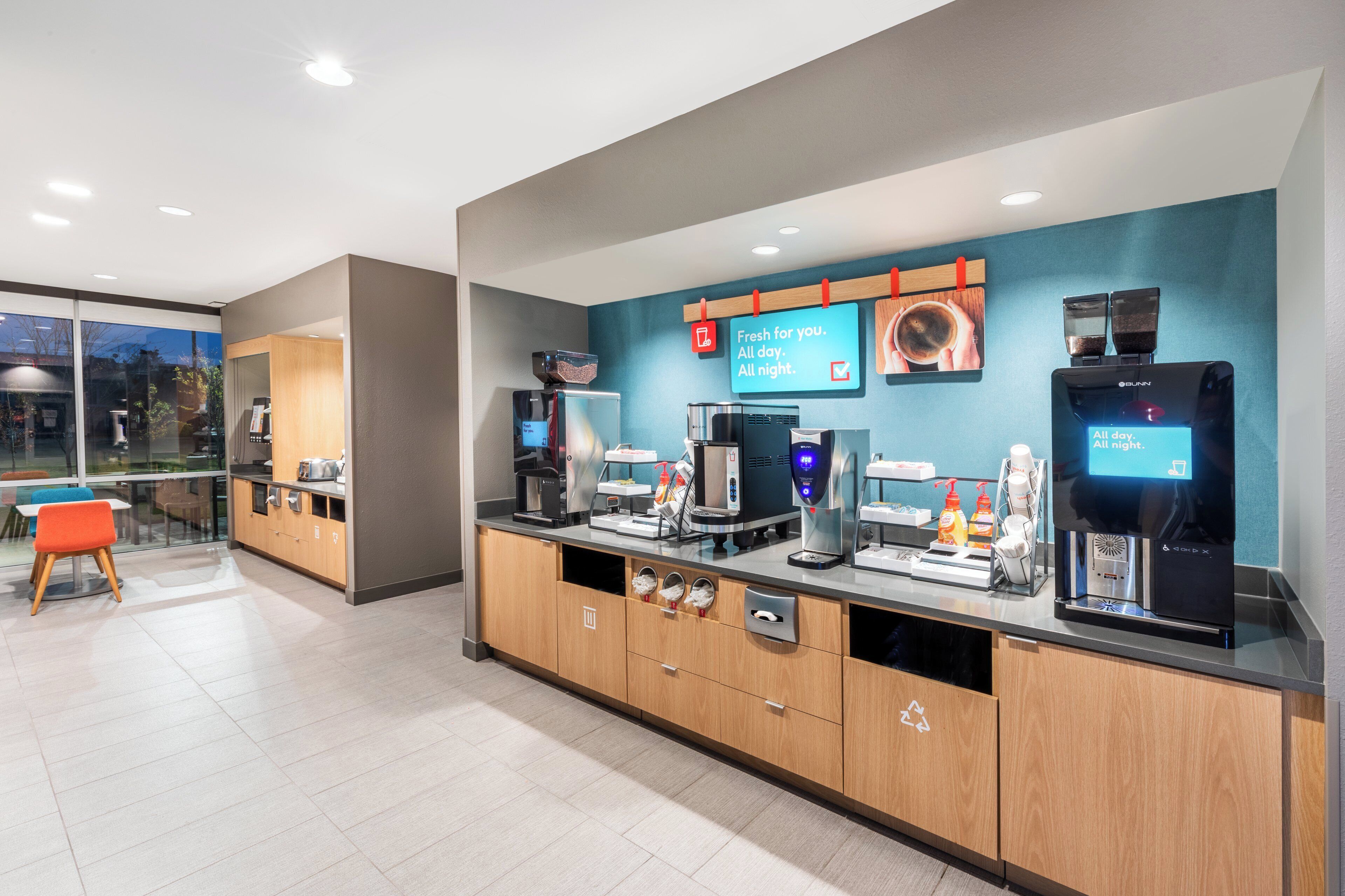 A modern cafe with a coffee machine, a menu board, and a seating area with chairs.