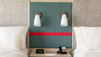 A hotel room with two beds, a nightstand with a digital clock, a telephone, and wall-mounted lamps.