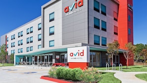 A modern building with the 'avid' logo and 'AN IHG HOTEL' text, featuring a flat facade, multiple windows, and a covered entrance area. - avid hotel Bentonville – Rogers by IHG (Bentonville)