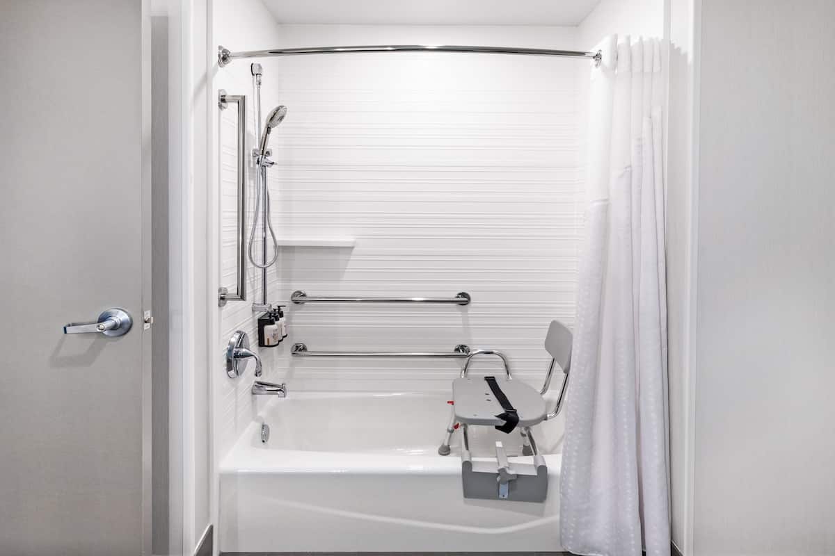 Une salle de bain moderne équipée d’une baignoire, d’une douche et de barres d’appui.