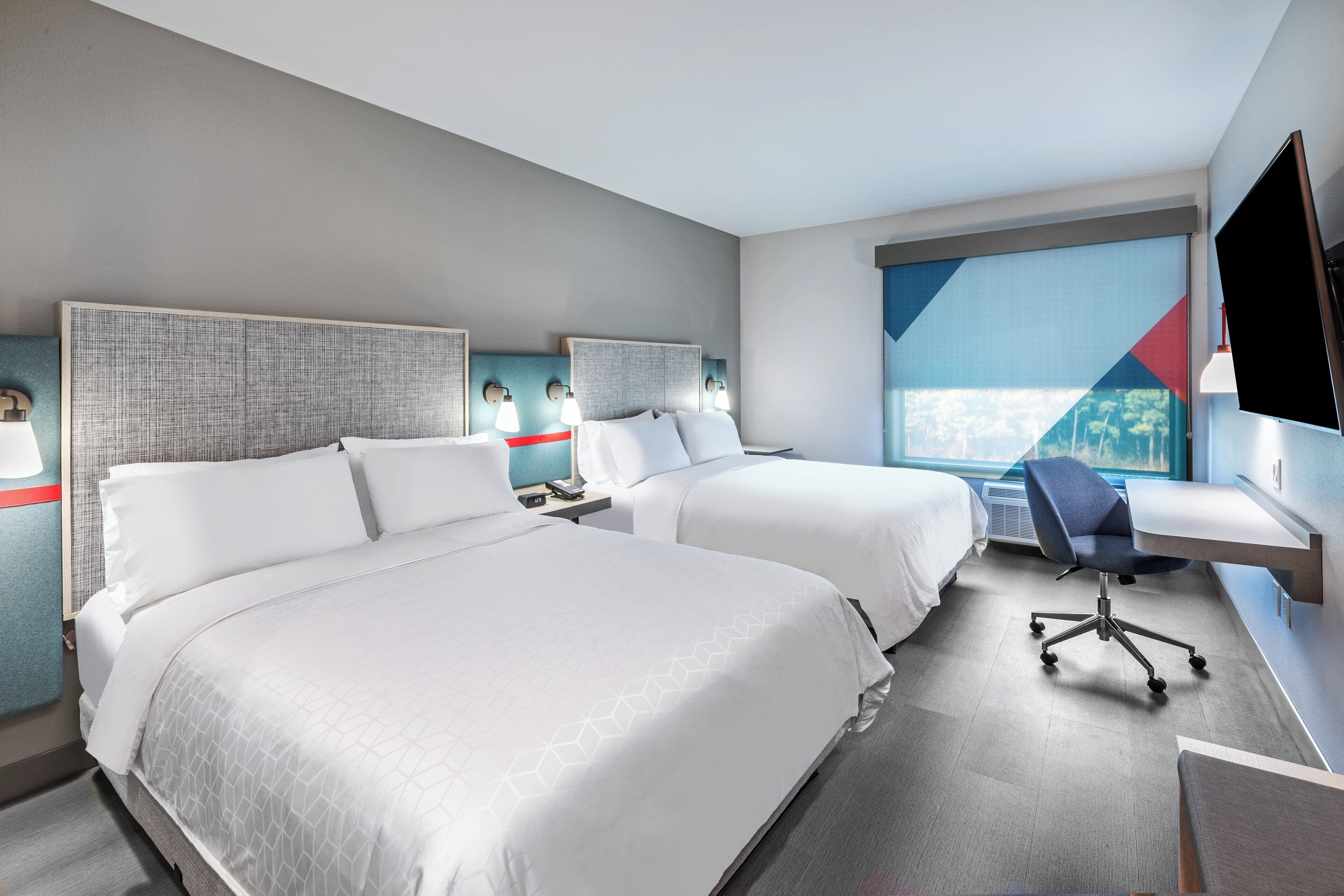 Habitación de hotel con dos camas, un escritorio, una silla y un televisor.