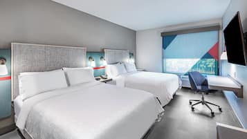 A hotel room with two beds, a desk, a chair, and a TV.