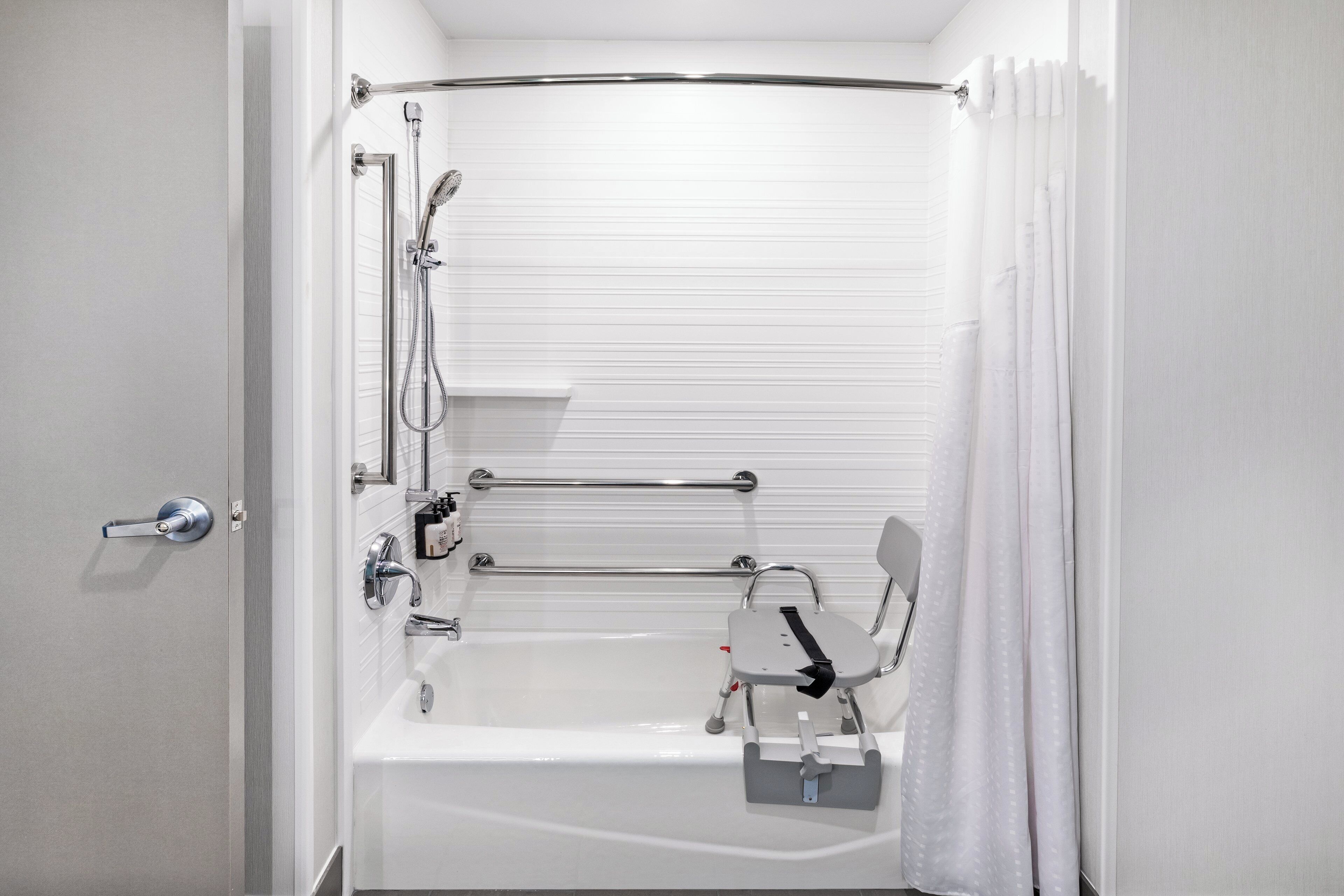 Une salle de bain moderne équipée d’une baignoire, d’une douche et de barres d’appui.