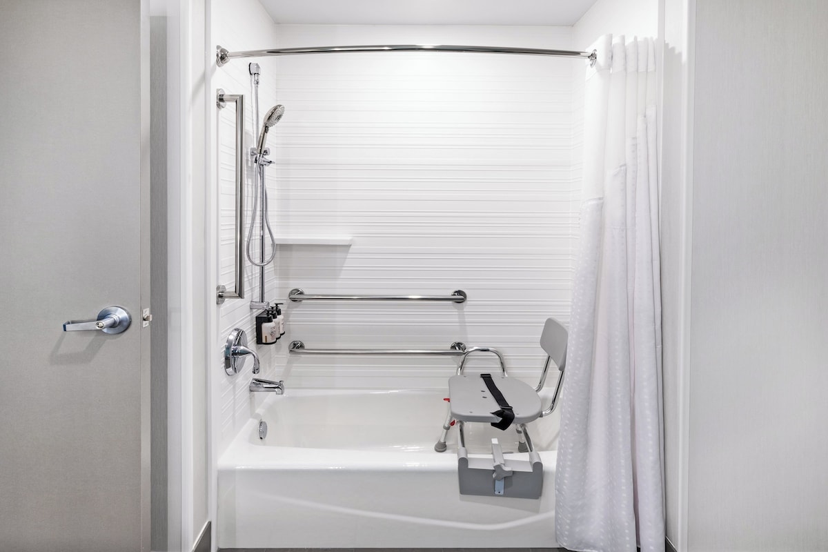 A modern bathroom with a bathtub, shower, and handrails.