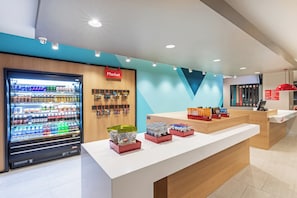 Un espacio comercial moderno con máquina expendedora, exhibición de snacks y un mostrador de recepción.