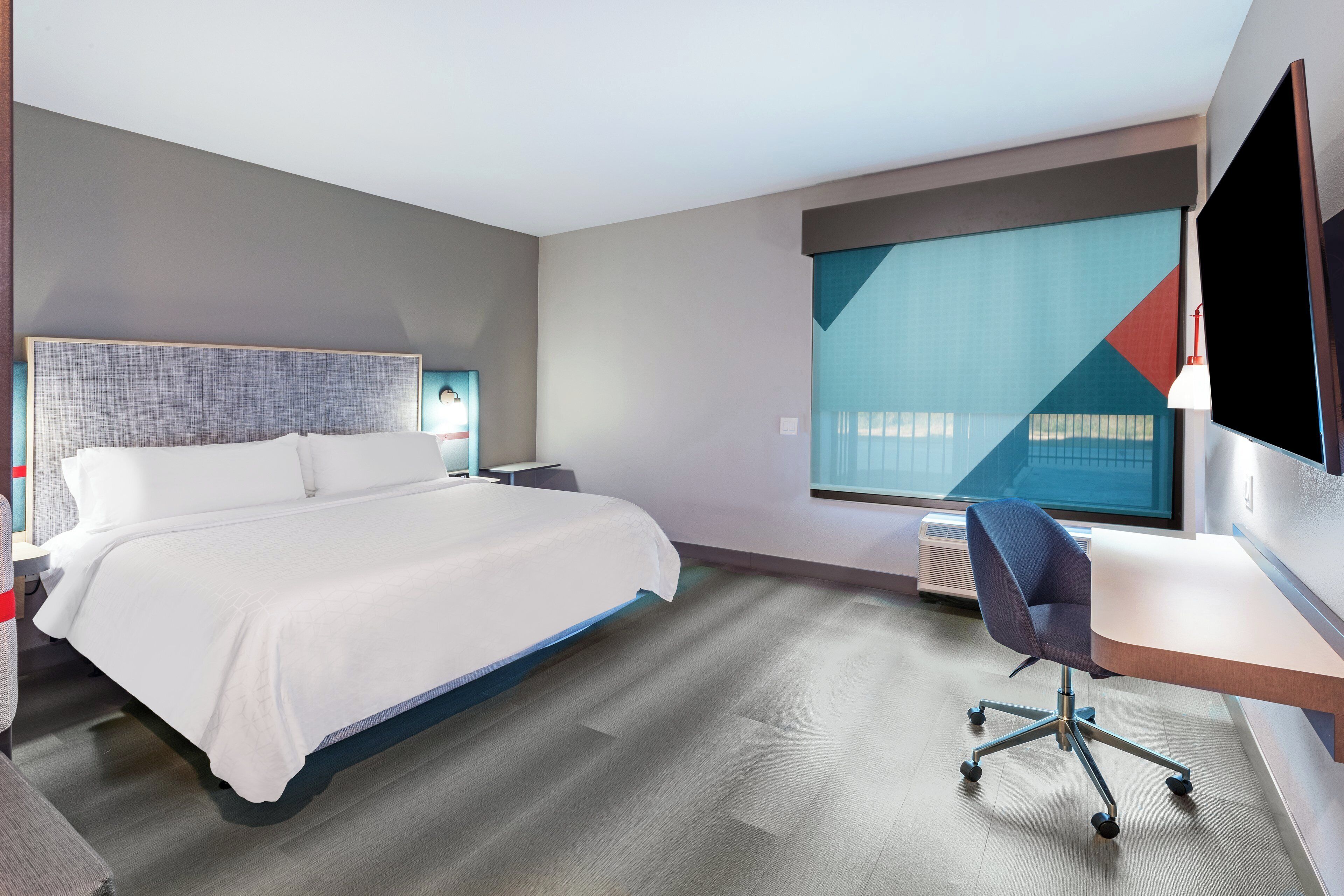 A modern hotel room with a large bed, a desk, and a television.