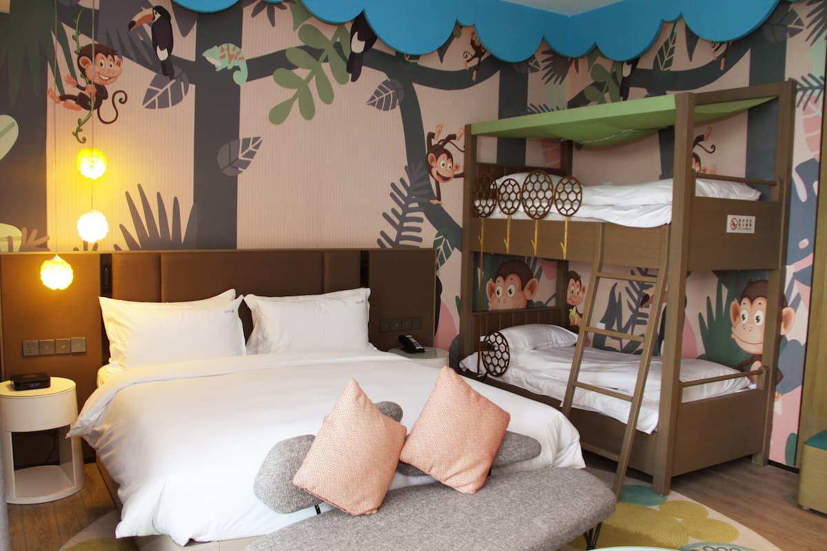 Una habitación de hotel con una cama doble, una cama individual y una mesita de noche con una lámpara.