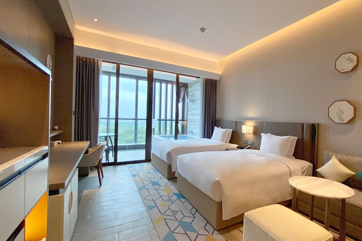 Habitación de hotel con dos camas, un escritorio, un sofá y un balcón con vistas.