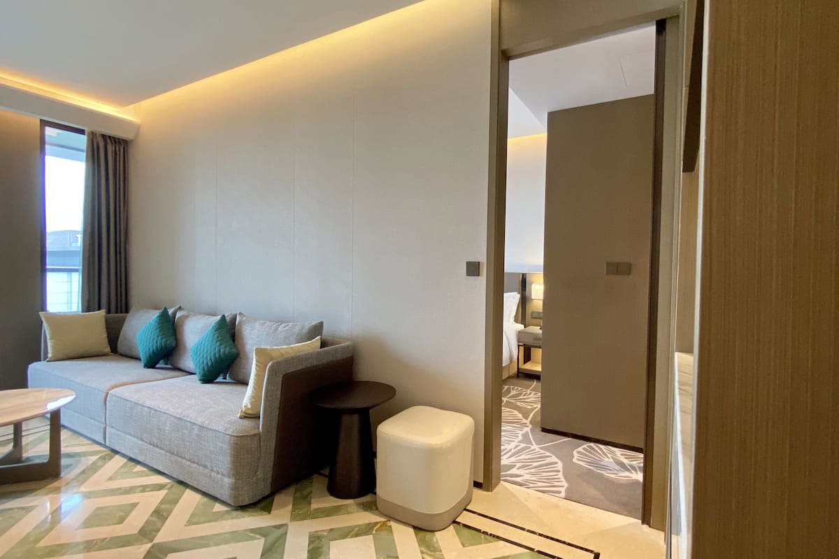 Una habitación de hotel moderna con un sofá, una mesita y una silla. Se ve una puerta que da a otra habitación.