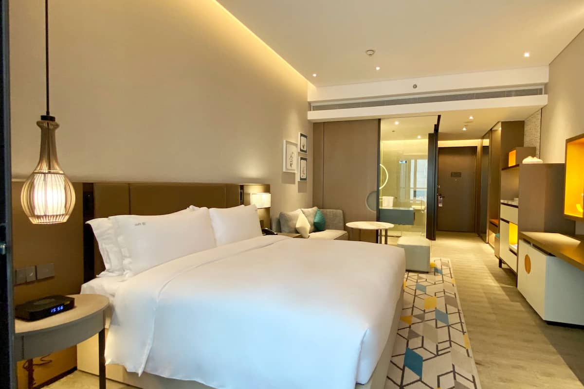Una habitación de hotel moderna con una cama grande, mesitas de noche, un escritorio, un televisor y un baño visible a través de una puerta abierta.