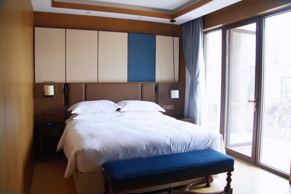 Habitación de hotel con una cama grande, una mesita de noche y una ventana con vistas, además de una puerta corrediza al balcón.