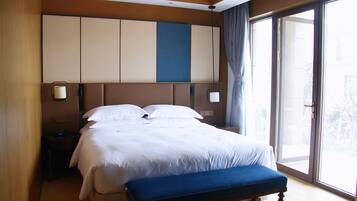 A hotel room with a large bed, a bedside table, a nightstand, a window with a view, and a sliding door to the balcony.