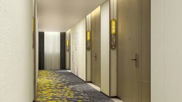 Corredor de hotel com carpete estampado, portas numeradas e luminária vertical.