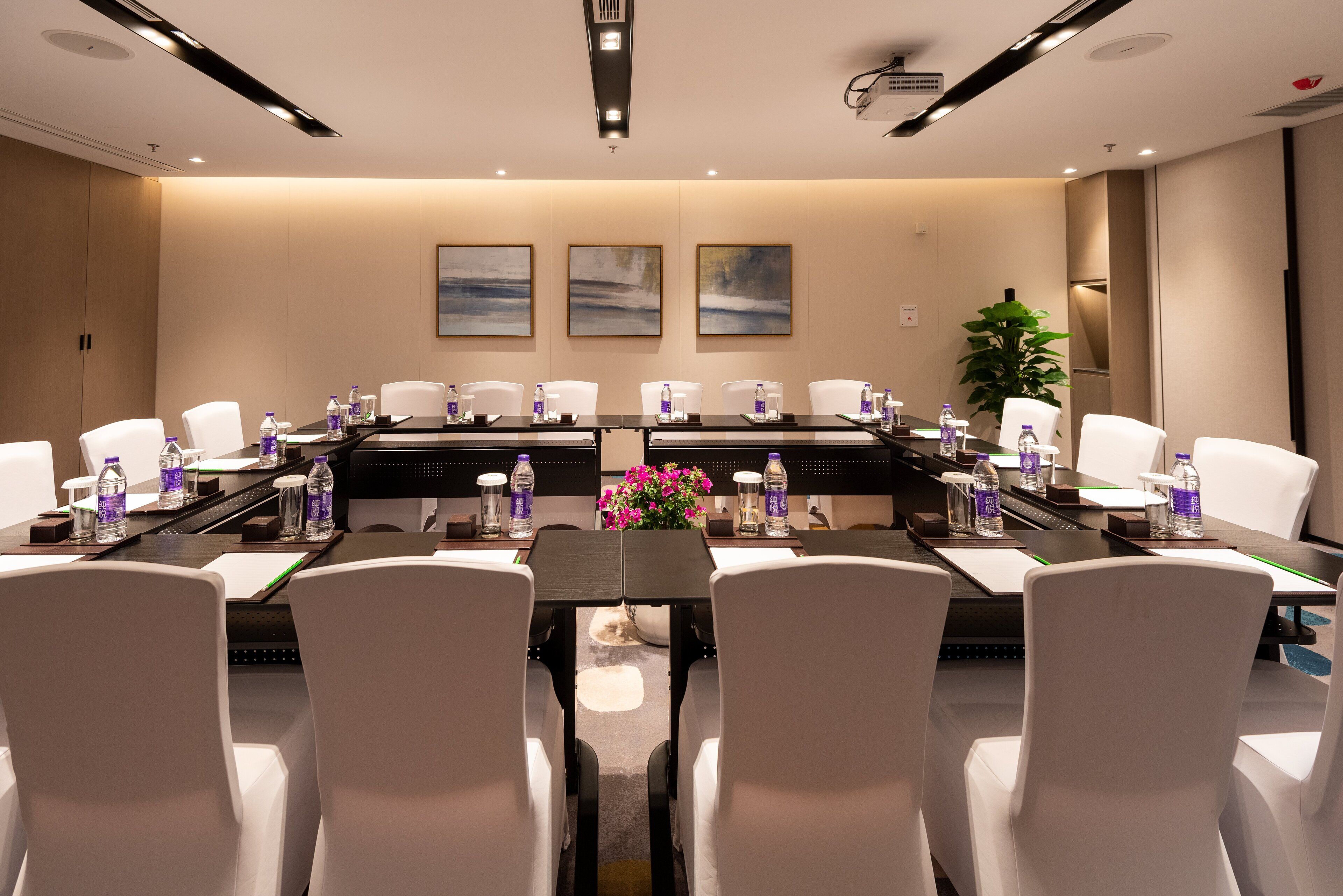A conference room with a long table, white chairs, water bottles, and a flower centerpiece.