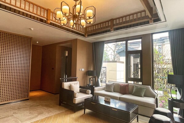A spacious living room with a sofa, armchair, and coffee table, a large window with a view, and a traditional ceiling design. - Holiday Inn Resort Maoshan Hot-Spring by IHG (Zhenjiang)