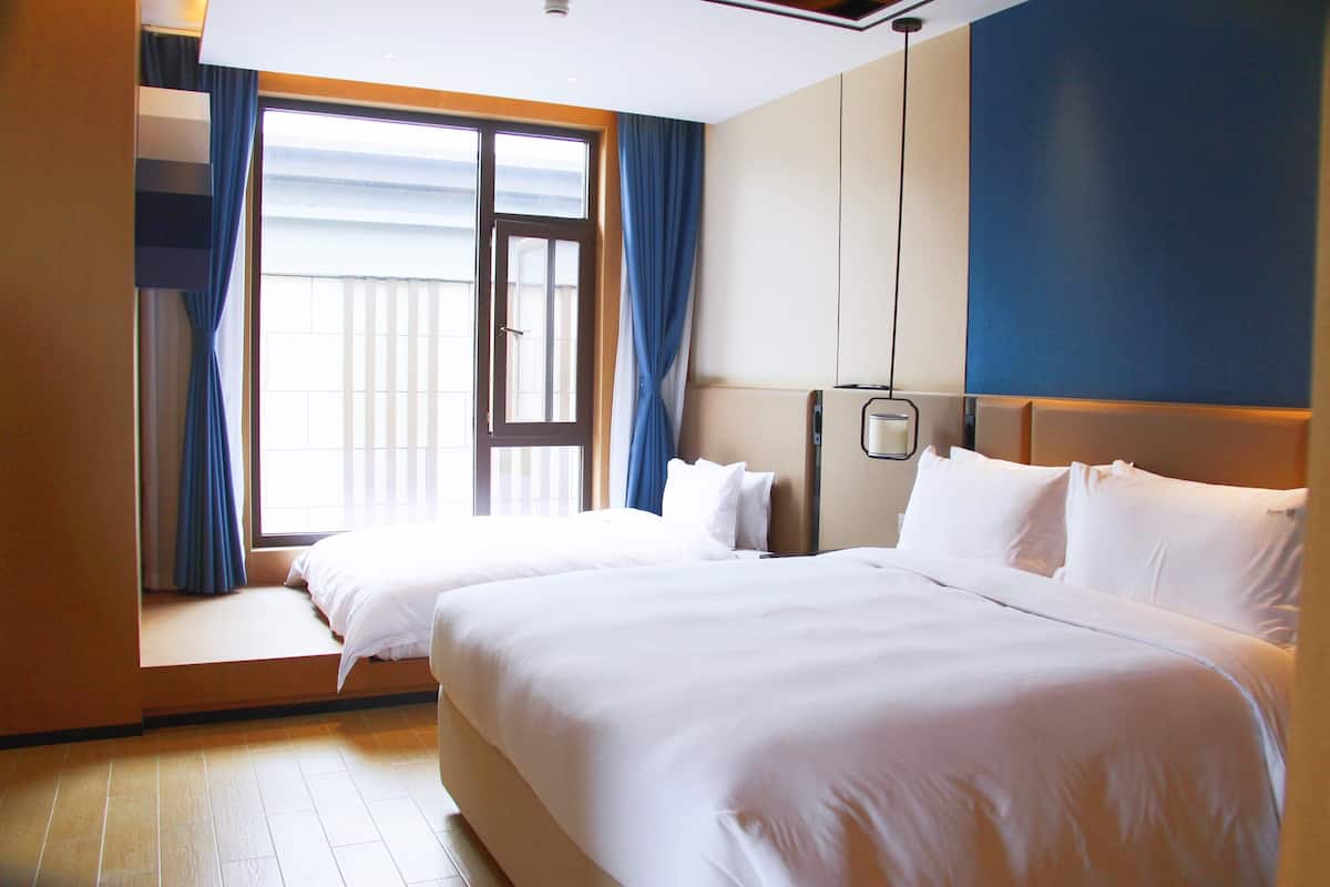 Habitación de hotel con dos camas, un ventanal con cortinas y vistas al exterior.