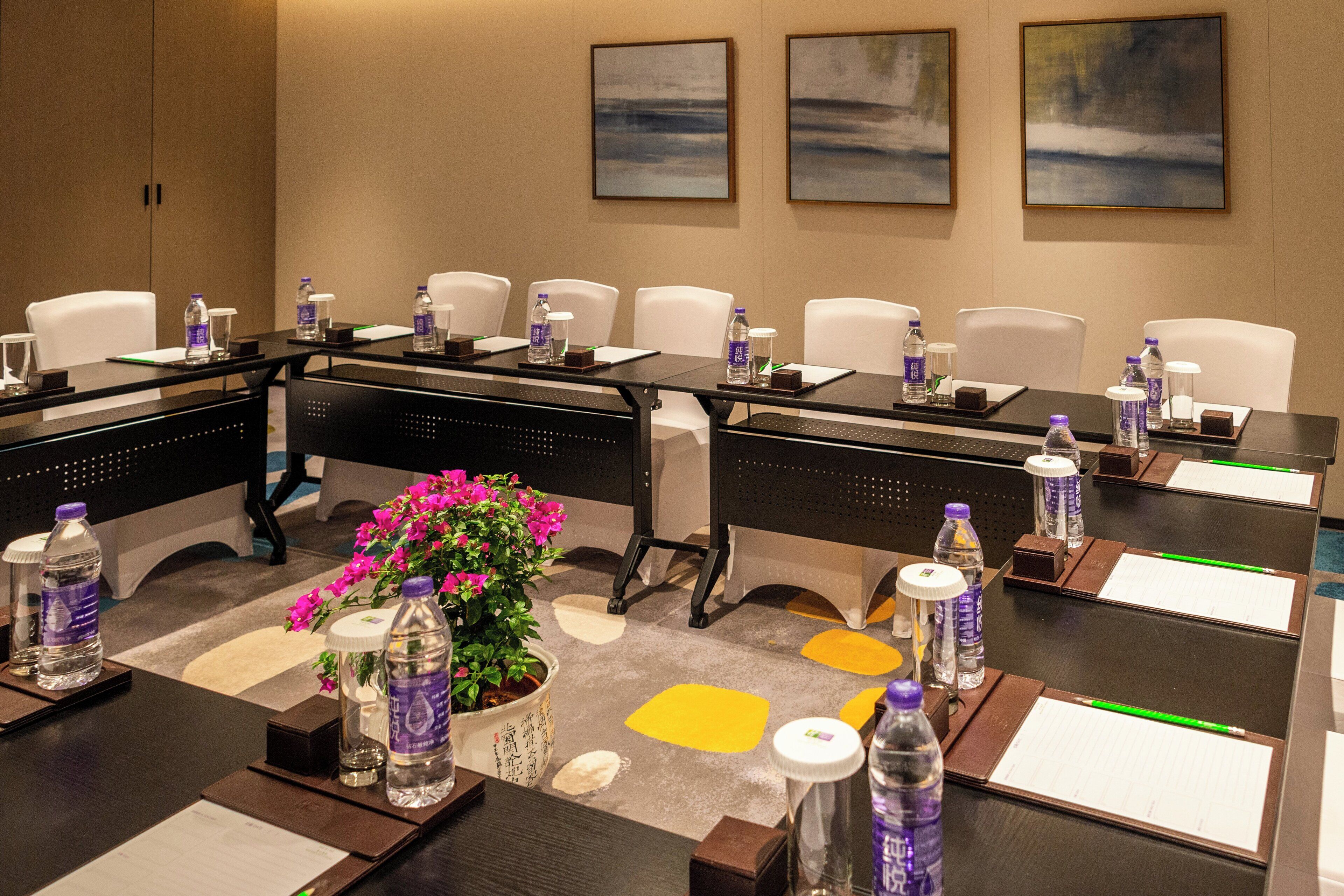 A conference room with a long table, chairs, water bottles, notepads, pens, and a potted plant.