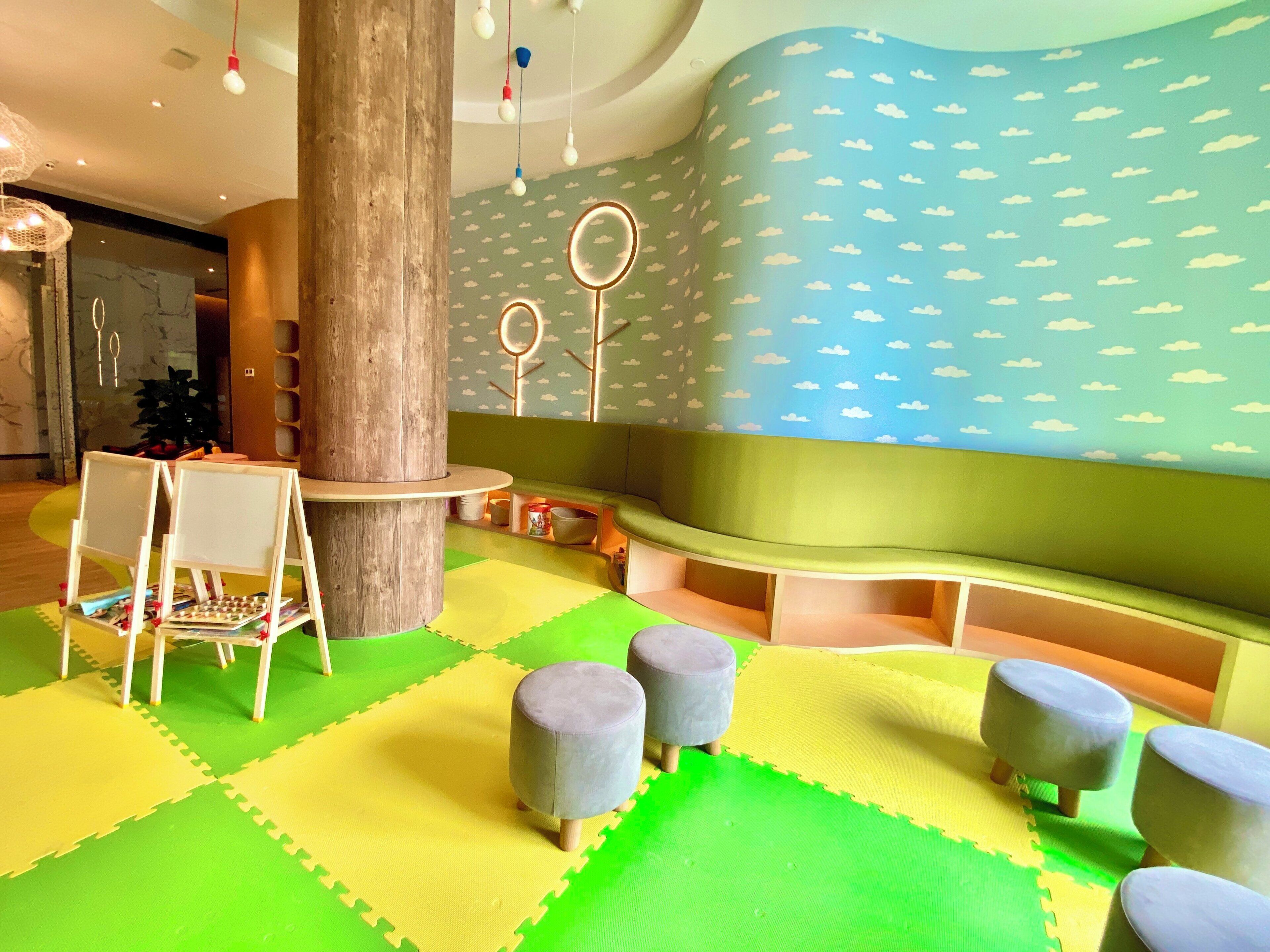 A children's play area with a wooden play structure, seating, and a wall with a cloud pattern.