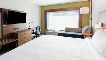 A hotel room with a bed, desk, chair, television, window, and lamp.