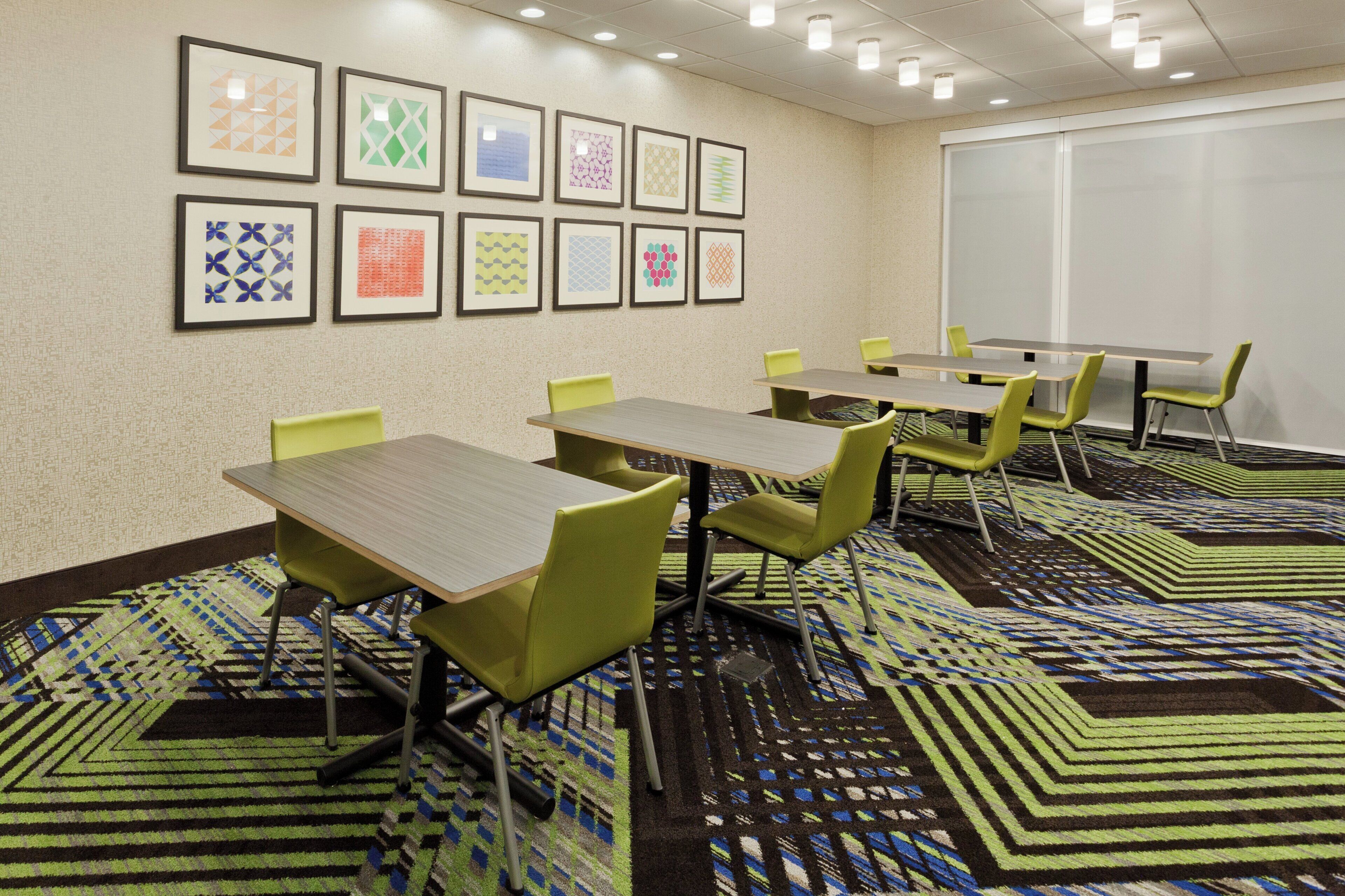 A conference room with tables and chairs, patterned carpet, and framed artwork on the wall.