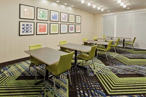 A conference room with tables and chairs, patterned carpet, and framed artwork on the wall.