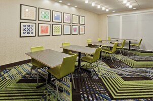 Una sala de conferencias con mesas y sillas, alfombra estampada y cuadros en la pared.