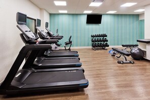 Un gimnasio con cintas de correr, mancuernas y pelotas de ejercicio.
